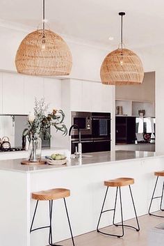 a kitchen with three stools in front of the counter and two hanging lights above it