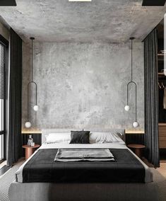 a bedroom with concrete walls, black and white bedding, two hanging lights and a large window