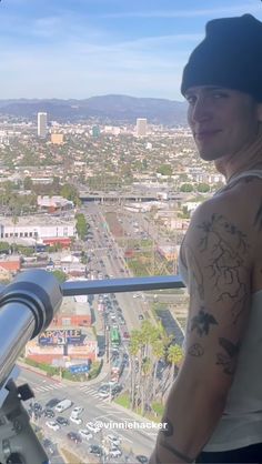 a man with tattoos on his arm standing in front of a window overlooking a city