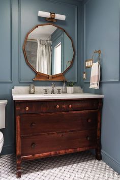 a bathroom with blue walls and a wooden dresser in front of a mirror on the wall