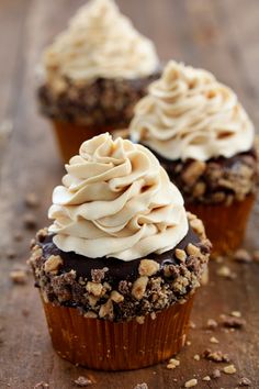 three cupcakes with frosting and walnuts on a wooden table, ready to be eaten