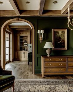 a living room with green walls and wooden furniture in the center, along with an arched doorway leading to another room