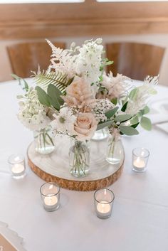 a vase filled with white flowers and greenery on top of a wooden table next to candles