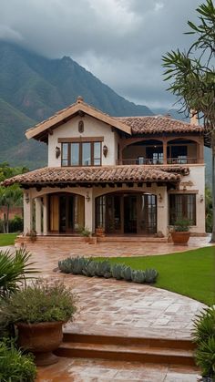 a large house sitting in the middle of a lush green field with mountains in the background