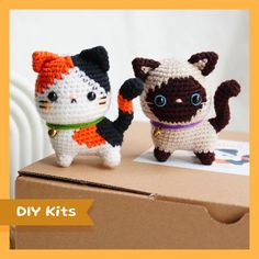 two small crocheted cats sitting on top of a cardboard box next to each other