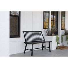 a wooden bench sitting in front of a white building next to two potted plants