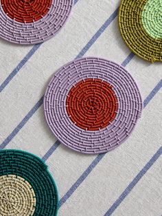 four woven coasters with different colors and designs on them sitting on a striped tablecloth