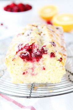 a close up of a piece of cake on a wire rack with berries and lemons in the background