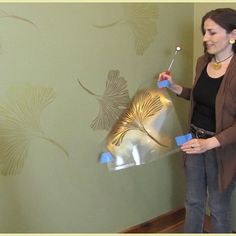 a woman holding a paint roller and painting a wall with gold leaf designs on it