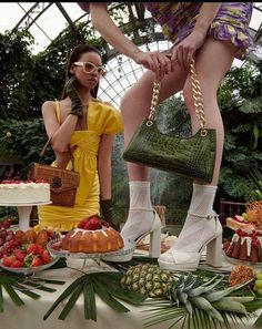 two women in high heels standing next to a table full of fruit and cake items