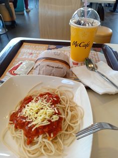 a white plate topped with spaghetti and sauce next to a drink on a table top