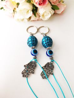 two key chains with blue beads on them and flowers in the backgroung