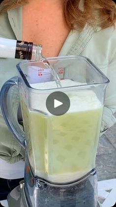 a woman is pouring some liquid into a blender to make something green and white