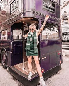 a woman standing on the steps of a double decker bus with her arms in the air