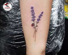 a woman's arm with purple flowers and ladybug tattoo on the left forearm