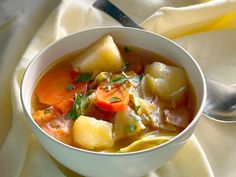 a white bowl filled with vegetable soup on top of a yellow cloth next to a spoon