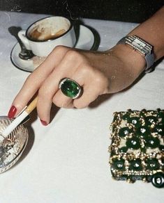 a woman's hand with a ring on her finger next to a cup of coffee