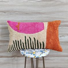 a colorful pillow sitting on top of a wooden table next to a chair and stool