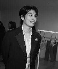 black and white photograph of a man in a suit smiling at the camera while standing next to clothes on hangers