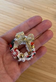 a hand holding a small christmas wreath with bells on it's front and side