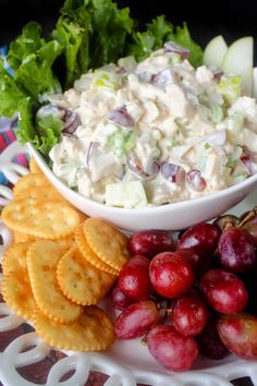 a plate with grapes, crackers and salad on it