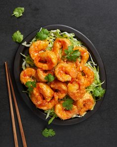 a black plate topped with shrimp and lettuce next to chopsticks