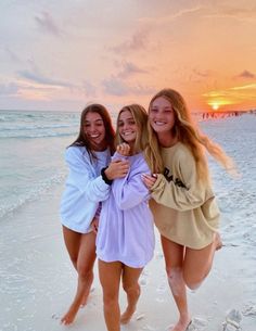 three girls are posing on the beach at sunset