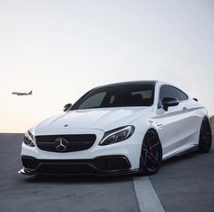 a white car parked in a parking lot next to an airplane