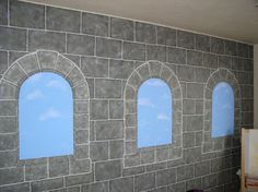 three windows in a stone wall with blue sky painted on them and one window is open