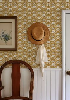 a hat is hanging on the wall next to a wooden chair and framed painting in a room