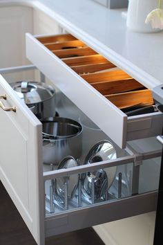 an open drawer in a kitchen with pots and pans on the bottom shelf,