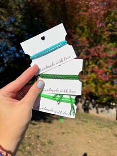 someone is holding three small tags with green string attached to them in front of some trees