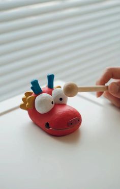 a hand holding a toothbrush over a red toy animal with horns and nose shaped like a giraffe