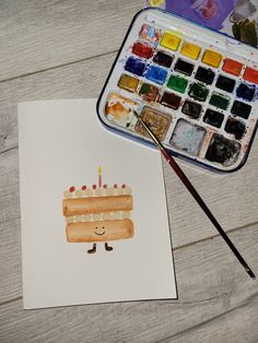 a piece of paper with a cake on it next to a paintbrush and watercolor palette