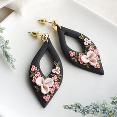 two pairs of black and pink flowered earrings sitting on top of a white plate