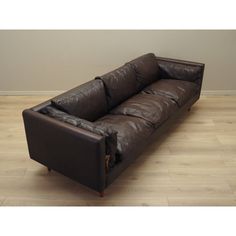 a brown leather couch sitting on top of a hard wood floor next to a wall