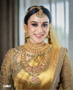 a woman in a gold and green bridal outfit with jewelry on her neck, smiling at the camera