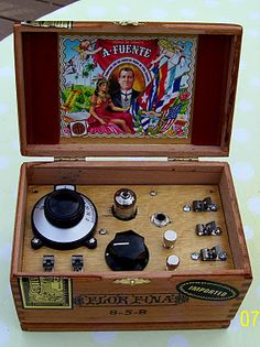 an open wooden box filled with assorted items sitting on top of a white table