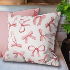 a white pillow with pink bows on it next to a potted plant and vase