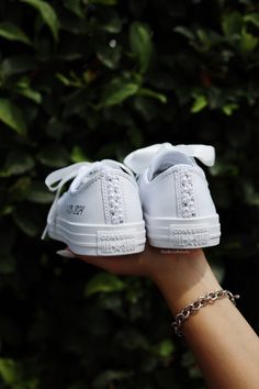 a woman's hand holding two white tennis shoes on top of each other with chains around them