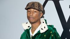 a man in a green jacket and hat standing next to a wall with letters on it