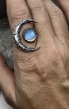 Witchy style crescent moon ring with a touch of blue moonstone. I have more of these gorgeous garnets in stock for custom orders. I have also made this ring with a blue moonstone, be sure to check my shop for the listing. Custom orders are welcome if you have a specific stone in mind. Feel free to contact me with any questions or comments. Ring Size. Made to order in your size. Moon Size. 1 inch in length and 3/4 inch Moonstone Size. 10mm Blue Moonstone Jewelry, Celestial Moonstone Ring With Moon Charm, Celestial Crescent Moonstone Ring, Bohemian Hand Forged Round Moonstone Ring, Mystical Moonstone Open Ring Jewelry, Celestial Moon Shaped Moonstone Crystal Ring, Celestial Moon-shaped Moonstone Crystal Ring, Unique Moonstone Crystal Open Ring, Moonstone Open Ring With Moon Phase Detail