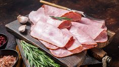 raw meats are displayed on a cutting board with herbs and spices around them, along with other ingredients