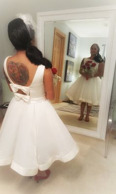 a woman in a white dress looking at herself in the mirror with her back to the camera