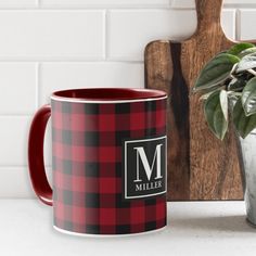 a red and black plaid coffee mug next to a cutting board with a potted plant