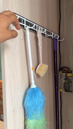 a person is holding a brush and broom in front of a wall mounted hook on a door