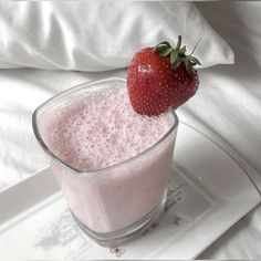 a strawberry sitting on top of a drink in a glass next to a white plate