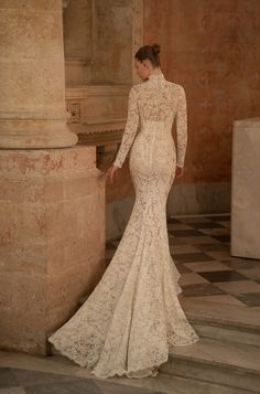 a woman in a long sleeved wedding dress standing next to a pillar and looking off into the distance