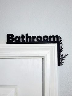 a bathroom sign hanging on the wall above a white door with black leaves and branches