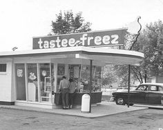 black and white photograph of two men standing in front of a fast food store with their luggage